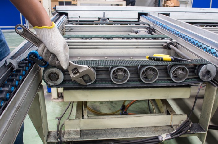 hand wearing a white glove tightening a part on a conveyor