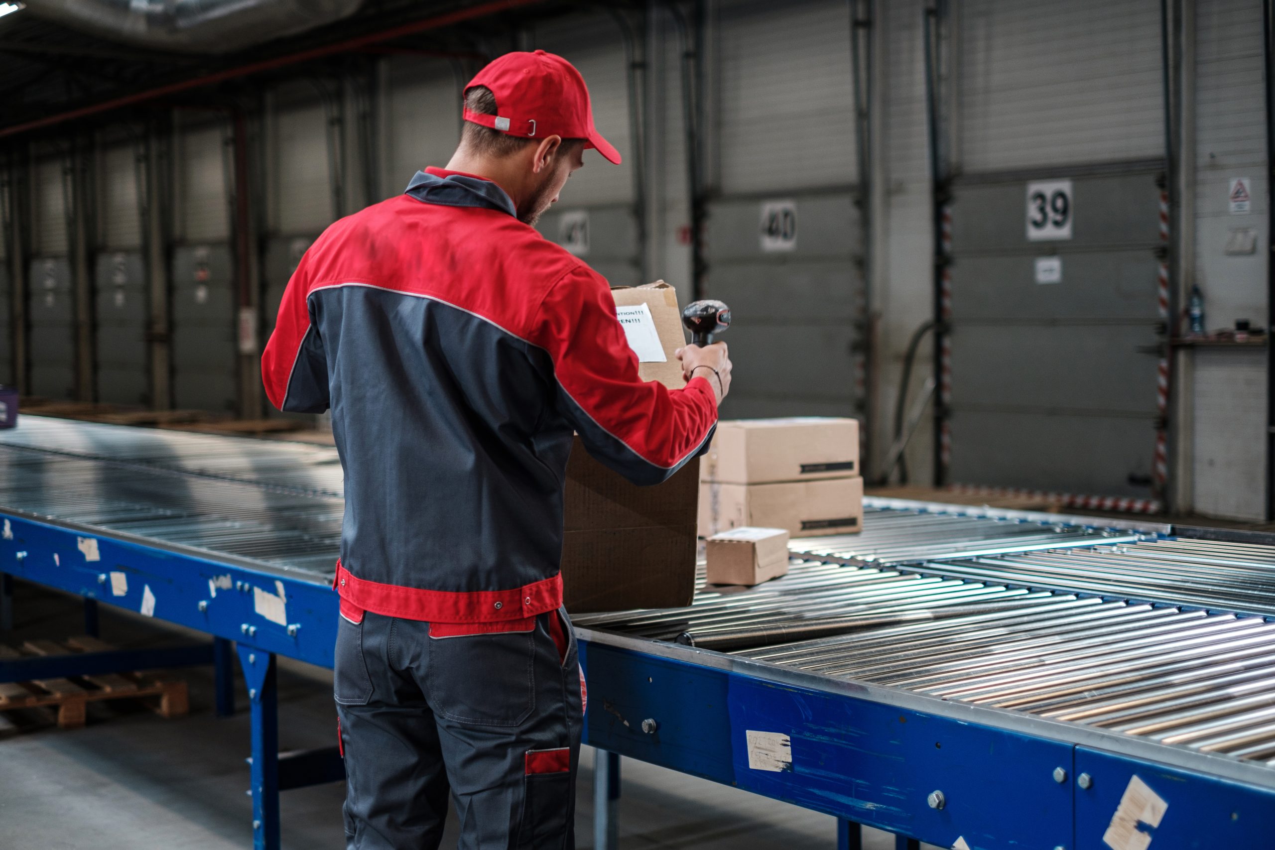 Worker with red jacket and hat standing beside a conveyor, working with boxes, showing how automation aids in successful logistics.